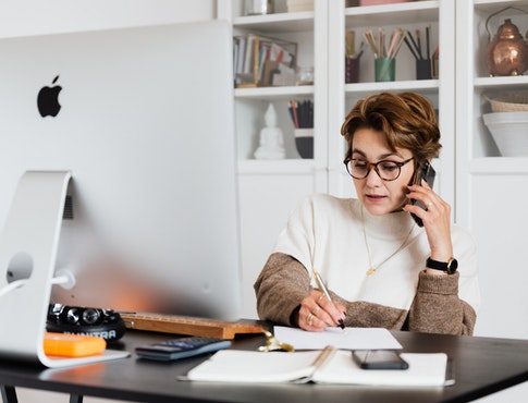 woman writing on note pad while on phone