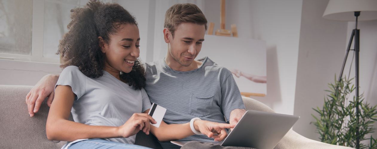 a young couple looking at a laptop with a credit or debit card in hand